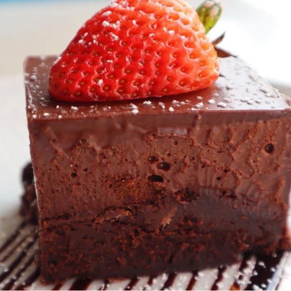 Rich chocolate cake with a fresh strawberry and powdered sugar, drizzled with chocolate sauce.