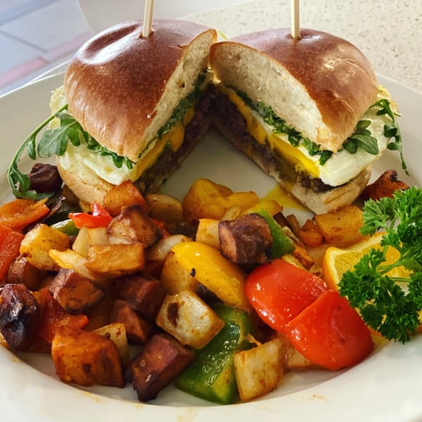 A breakfast burger with egg, cheese, and arugula, served with roasted potatoes and bell peppers.