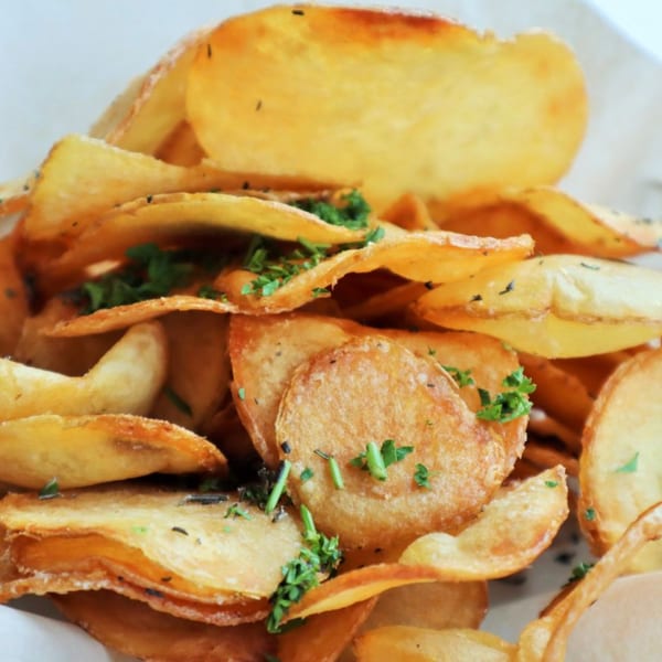 Golden-brown potato chips, lightly seasoned with herbs, piled high in a white bowl at Lulu California Bistro.