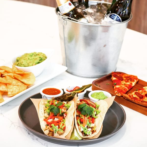 Tacos, pizza, guacamole, chips, and a bucket of beer on a white marble table at Lulu California Bistro.