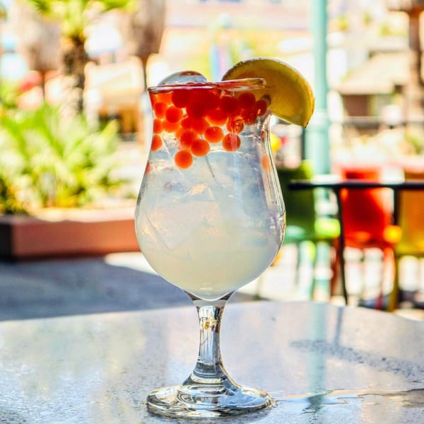 A refreshing cocktail with red boba pearls and a lemon slice, served on an outdoor patio table.